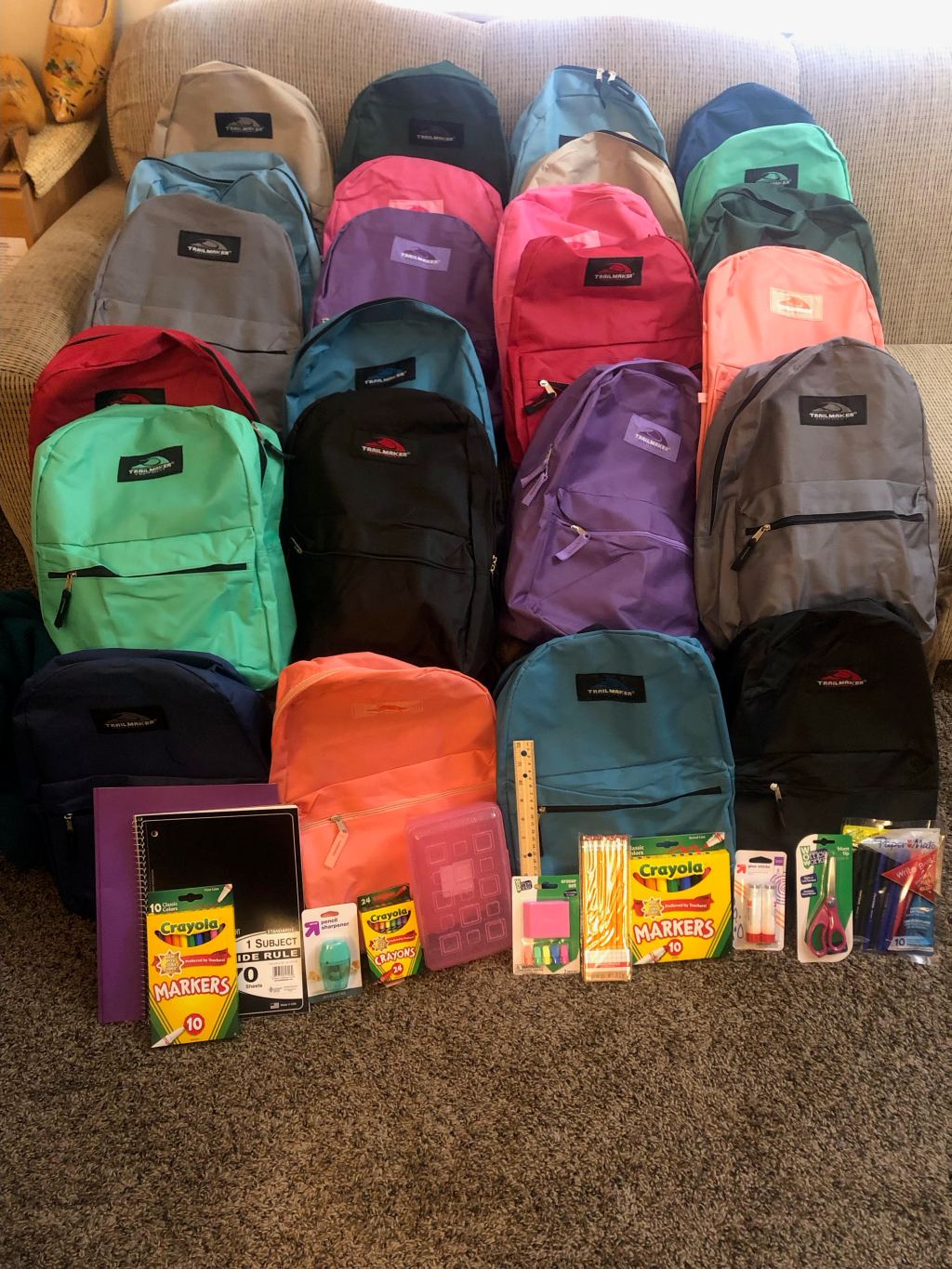 photo of 4 rows with 5 backpacks each. Front row shows art supplies, folders, and notebooks.