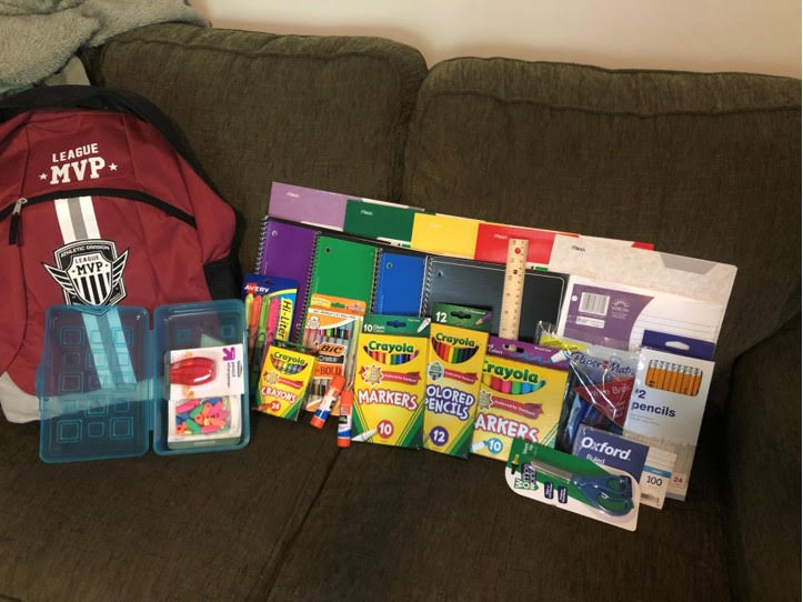 book bag on a sofa with school supplies next to it: art supplies, folders, notebooks