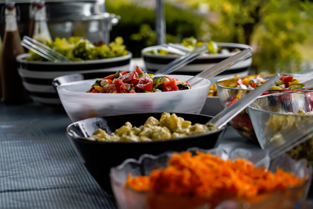 color photo of a table with bowls of salads and tongs