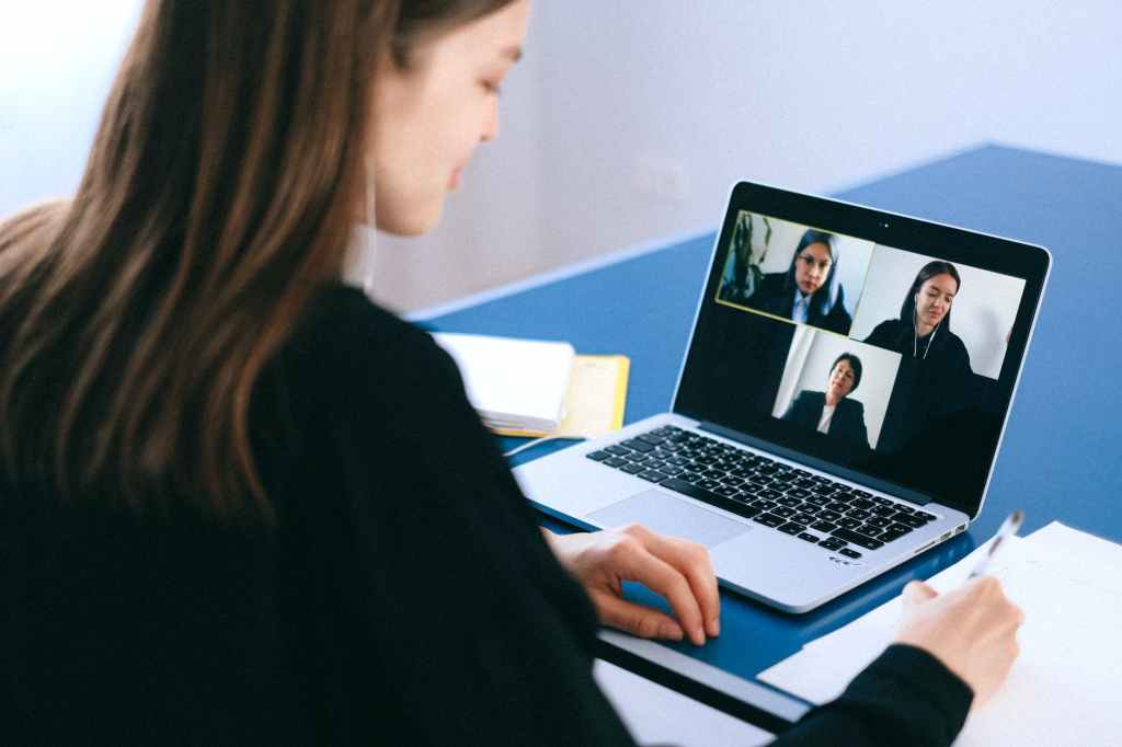 woman uses a laptop to join an online meeting with three others on the screen