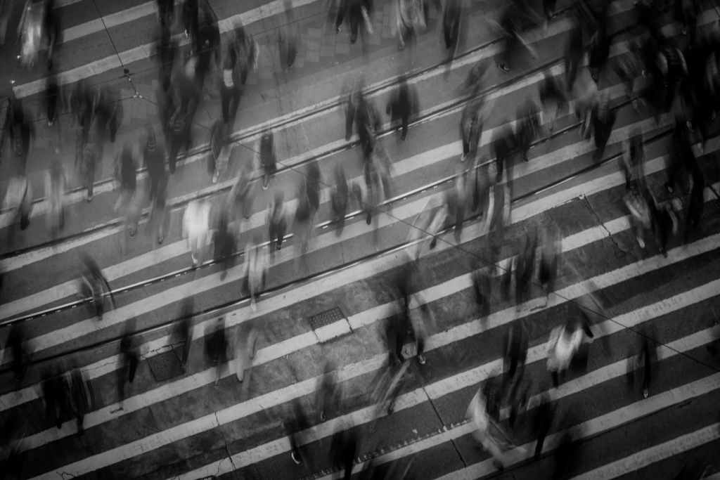 blurry black and white photo of many people crossing a busy intersection