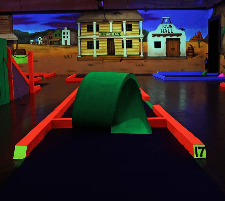 indoor mini golf loop the loop hole 17 with day glo green and orange colors. wild west paiting in background